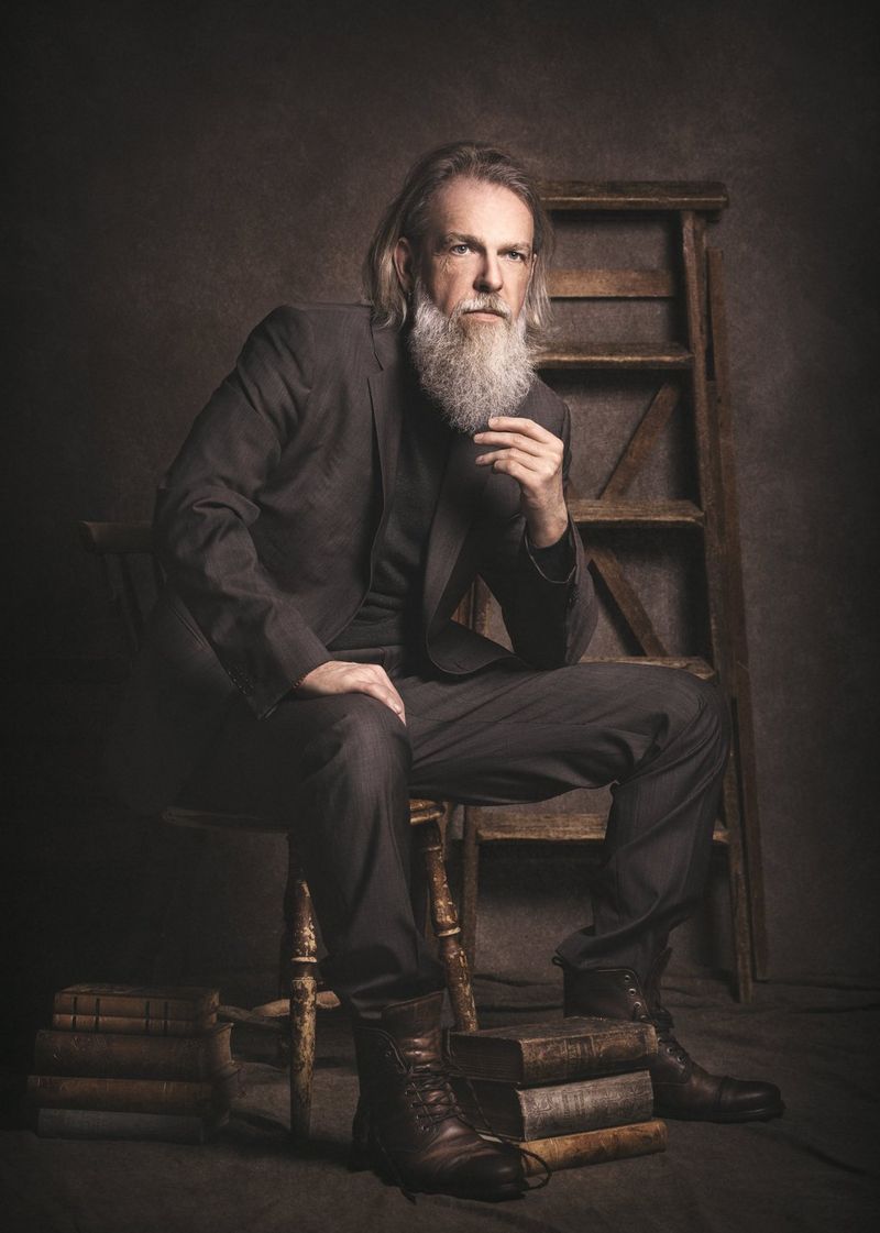 A fine art portrait of a man with a light-coloured beard sitting on a stool wearing a dark suit, taken by Martina Wärenfeldt on a Canon EOS R5. 