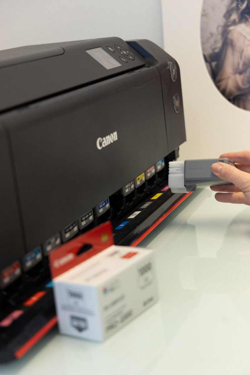 A hand replaces an ink cartridge in a Canon imagePROGRAF PRO-1000 printer. 
