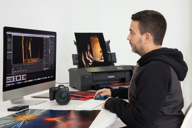 Photographer Joel Santos edits an image on his computer using Canon Professional Print & Layout software. Next to him are a Canon camera and A3 printer.  