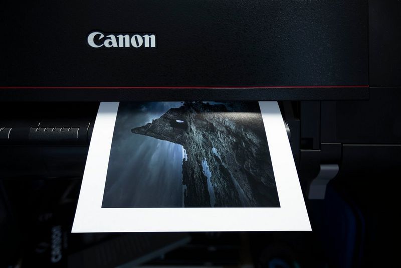 An A4 print of a rocky landscape with a thick white border emerges from a Canon printer. 