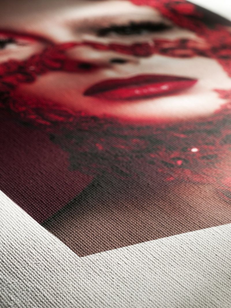 Een close-up van de hoek van een fotoprint op zwaar getextureerd papier, met hierop een bleek vrouwengezicht met helderrode lippenstift.
