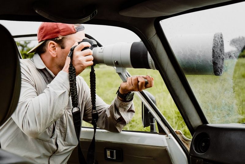 A photographer leans out of a vehicle in Murchison Falls National Park in Uganda. He is holding a Canon camera with a large telephoto lens.