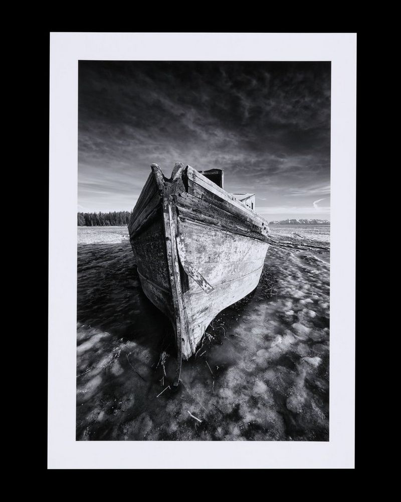 A black and white photograph, with a wide white border, of a beached boat.