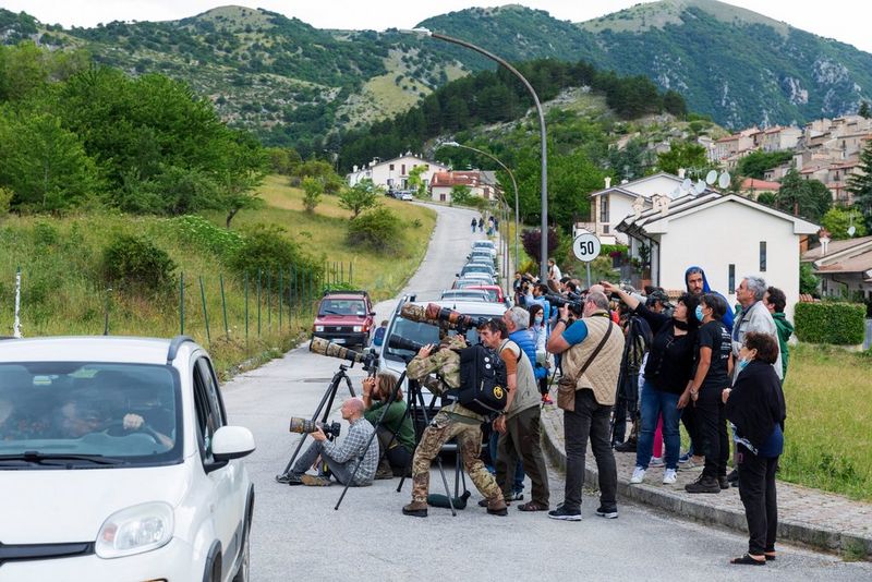 A crowd of photographers at the side of a road in a rural town.