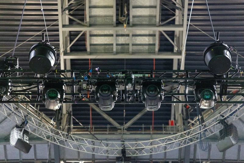 A view looking up at the lighting truss in the roof of a London arena, with a Canon PTZ camera just visible in the centre.