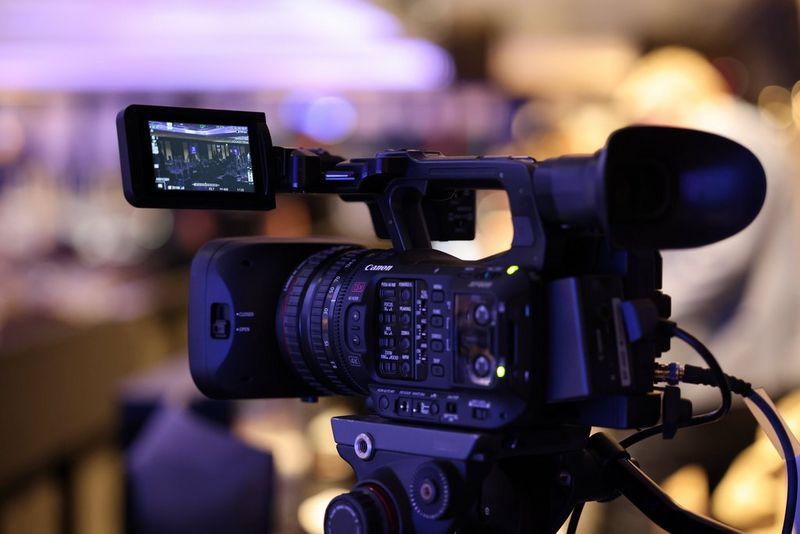 Ein Canon XF605 Camcorder auf einem Stativ, der Livebilder einer Bühnenszene auf dem LCD-Monitor zeigt.