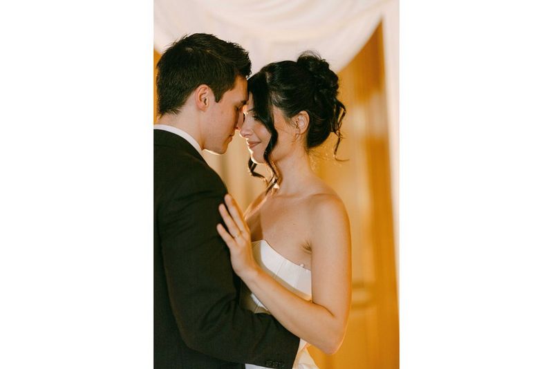 A romantic wedding portrait of a couple embracing in warm light indoors, taken with a Canon RF 85mm F1.4L VCM lens.