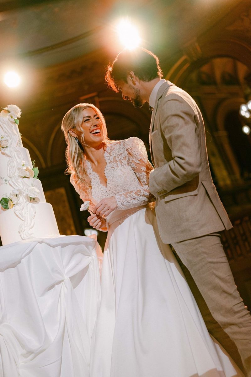 A wedding portrait of a couple standing next to a towering wedding cake, taken on a Canon EOS R5 Mark II with a Canon RF 50mm F1.4L VCM lens by wedding photographer Raïs De Weirdt.