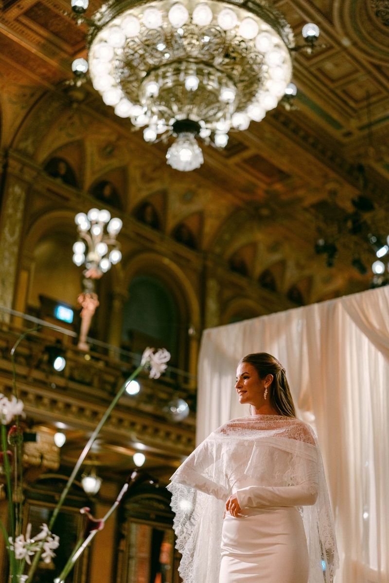 Low-angle shot of a bride in a large room, with background lights out of focus, taken on a Canon EOS R5 Mark II with a Canon RF 50mm F1.4L VCM lens by wedding photographer Raïs De Weirdt. 