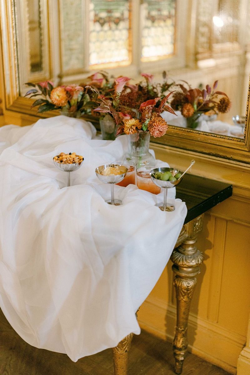 A detail shot of refreshments in metallic goblets on a bride's lace veil laid out on a side table under a mirror, taken on a Canon EOS R5 Mark II with a Canon RF 50mm F1.4L VCM lens by wedding photographer Raïs De Weirdt. 
