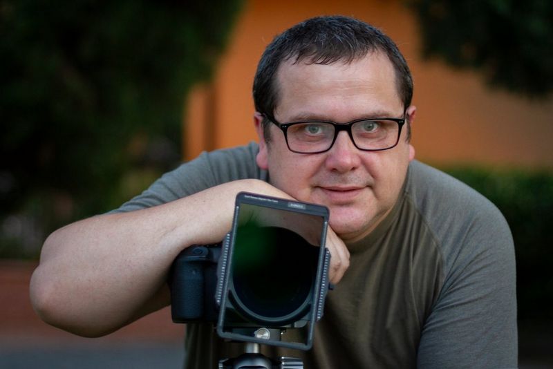 Un homme sourit en posant son bras sur son appareil photo monté sur un trépied.