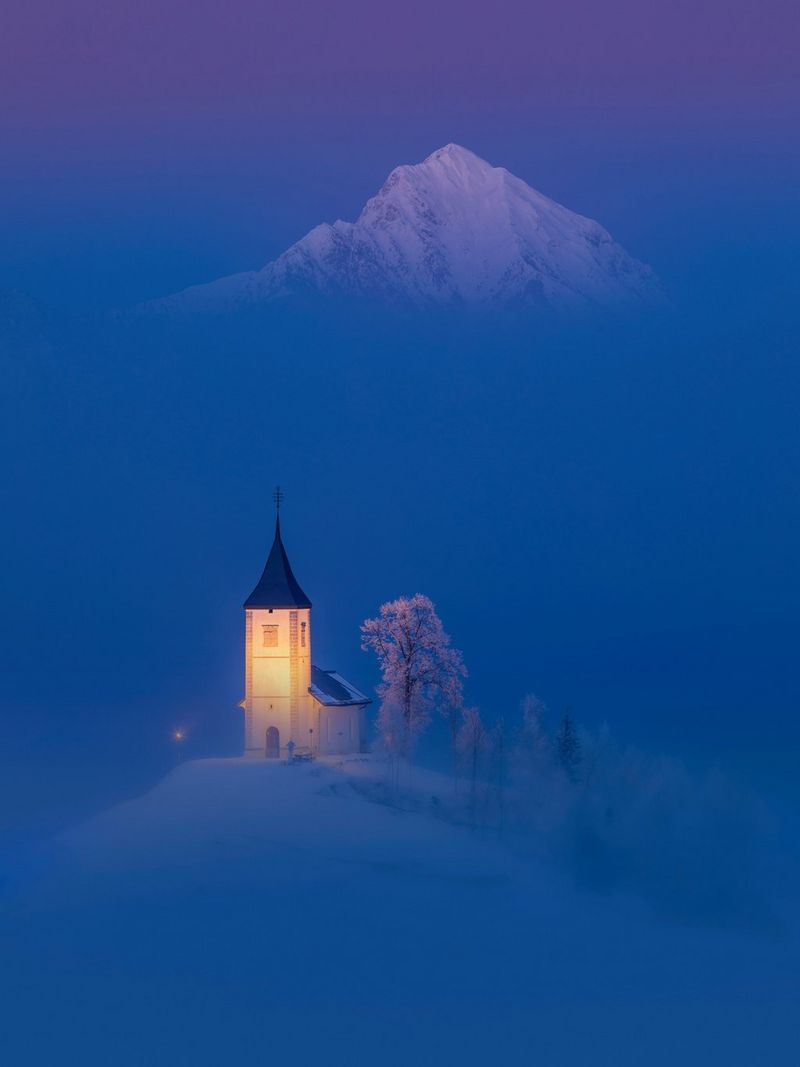 Une scène de faible luminosité d'une église illuminée dans un paysage enneigé. Un pic enneigé est juste visible en arrière-plan.