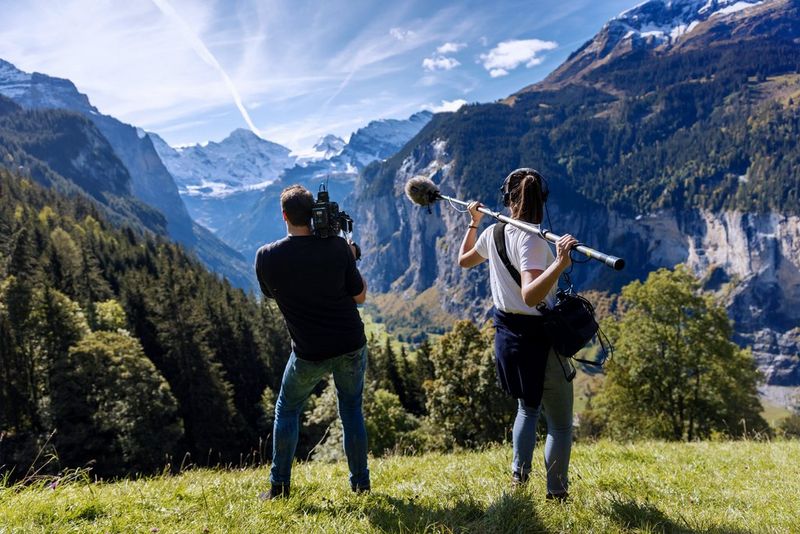 A man filming with a Canon camera and a woman holding a boom mic on a bright day in the Swiss Alps. 