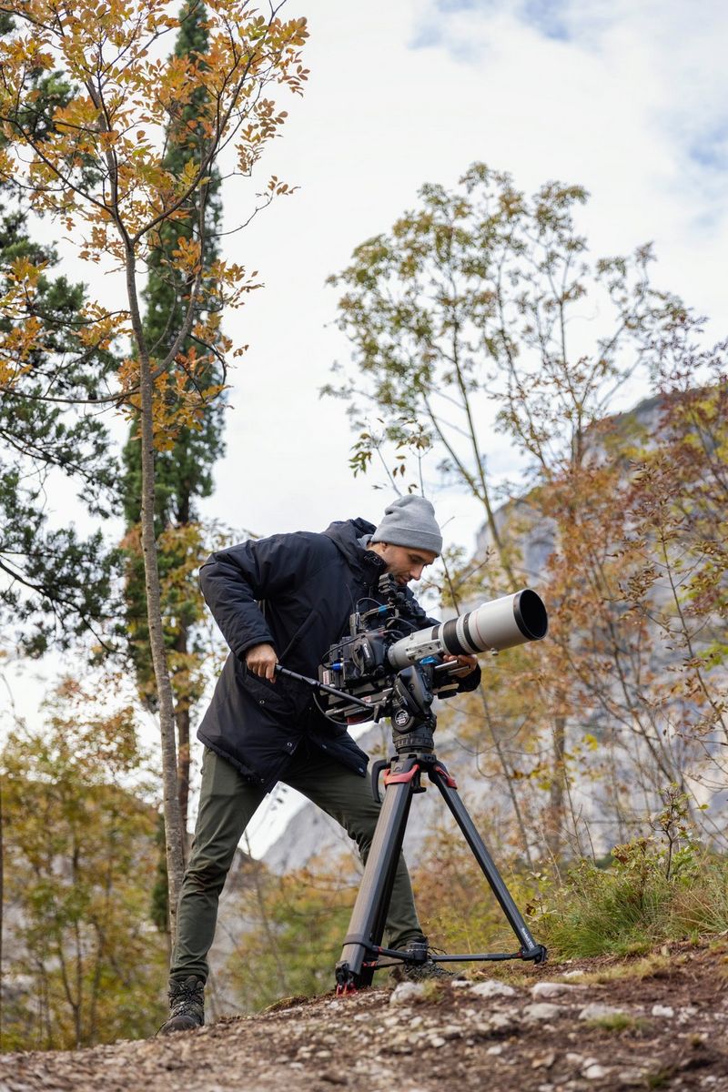 A man shooting with a Canon Cinema EOS camera and a telephoto lens on a tripod. 