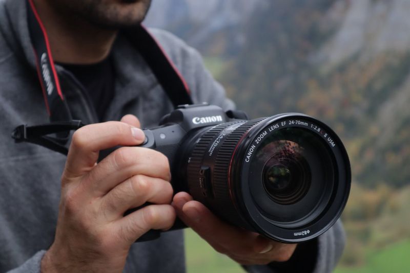 A man holding a Canon EOS R5 camera with an EF 24-70mm lens.