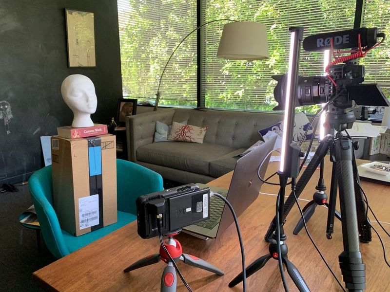 Testa di un manichino da negozio poggiata su una scatola su una sedia con un'attrezzatura per la ripresa con comando a distanza sul tavolo di fronte a essa.