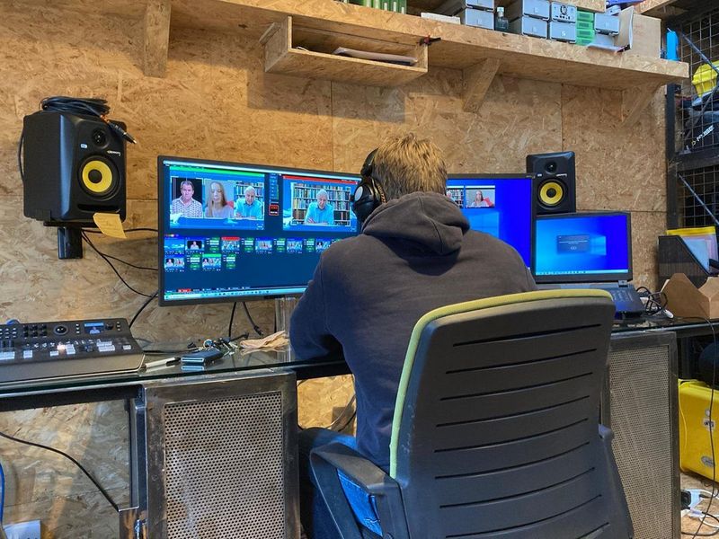 Uomo con le cuffie che monta interviste a personaggi di rilievo lavorando con tre monitor.