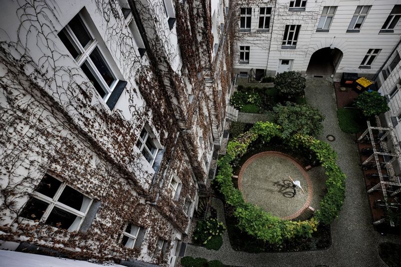 Photographié du dessus, un rider de BMX effectue une acrobatie sur un patio circulaire entouré de haies. Photo prise par Richard Walch avec un Canon EOS R5.