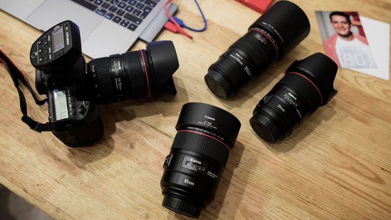 A Canon DSLR with a Canon EF 24-70mm f/4L IS USM lens on a desk alongside three other Canon lenses.