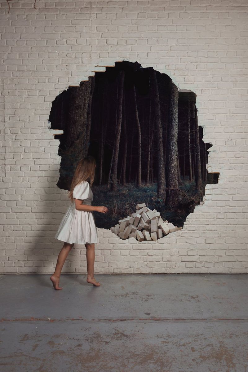 Photographer Rosie Hardy looks at an enchanted wood through a hole in a white-painted brick wall in a self portrait edited in Canon Digital Photo Professional.