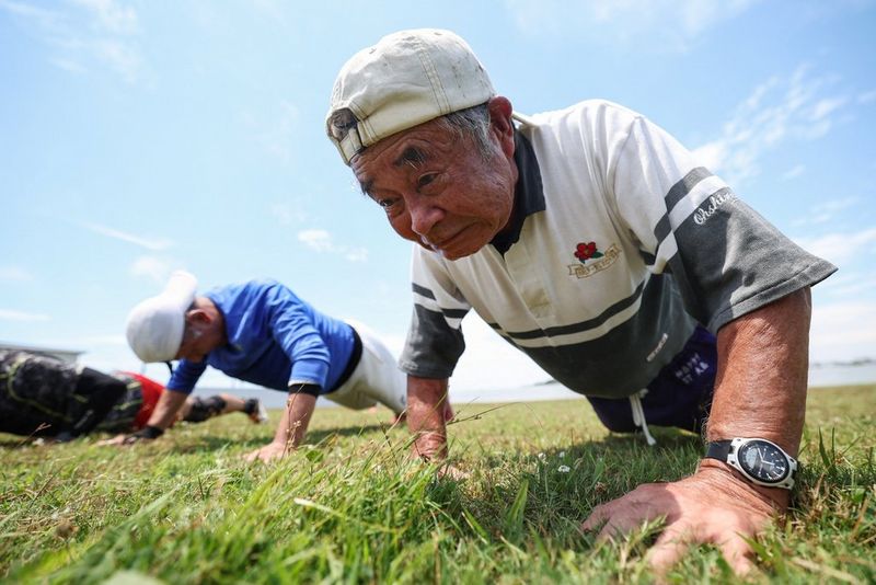Due uomini anziani, che fanno parte di una squadra di rugby della terza età in Giappone, con indosso cappellini bianchi, mentre eseguono flessioni su un campo erboso. Scatto realizzato con Canon EOS R3 e obiettivo Canon RF 15-35mm F2.8 L IS USM.