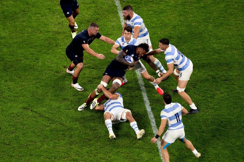 Un giocatore argentino che afferra l'avversario inglese per le ginocchia mentre i compagni di squadra di entrambi gli schieramenti si precipitano verso il pallone in una foto scattata alla Coppa del Mondo di rugby 2023 con una Canon EOS R3 da Tomás Francisco Cuesta