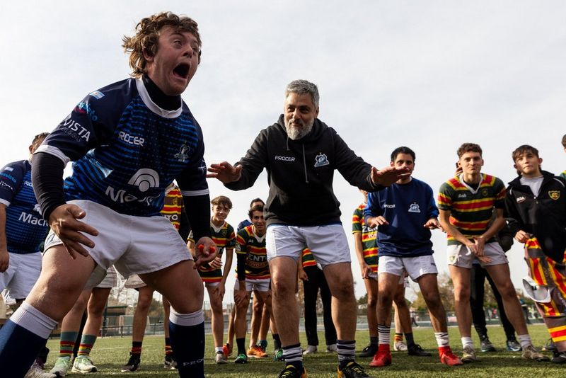 I membri della squadra di rugby inclusiva con abilità miste Pumpas XV e il loro allenatore mentre fanno qualche esercizio di riscaldamento. Un membro sembra gridare mentre è circondato dagli altri. Scatto realizzato da Tomás Francisco Cuesta con Canon EOS R6.