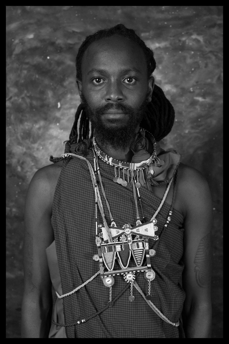 A black and white portrait of a man wearing a checked sarong and tribal-style jewellery.