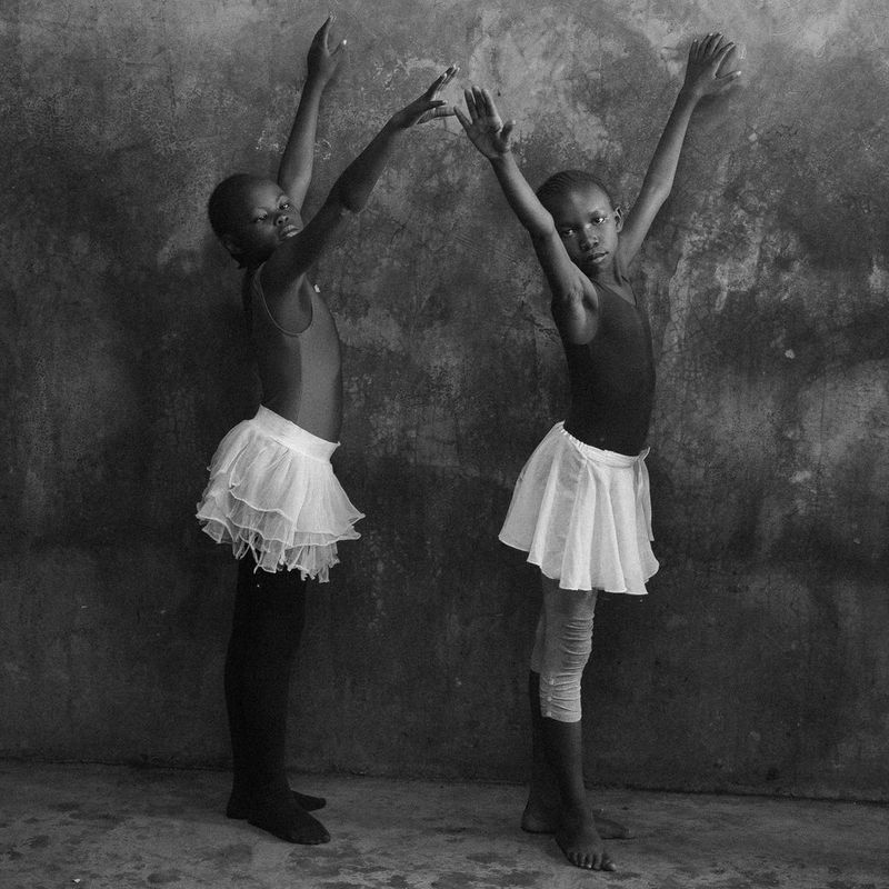 A black and white image of two young girls in ballet skirts, raising their arms above their heads.