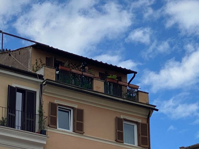 Un uomo fa una ripresa aerea dal balcone di un edificio color crema in una giornata di sole.