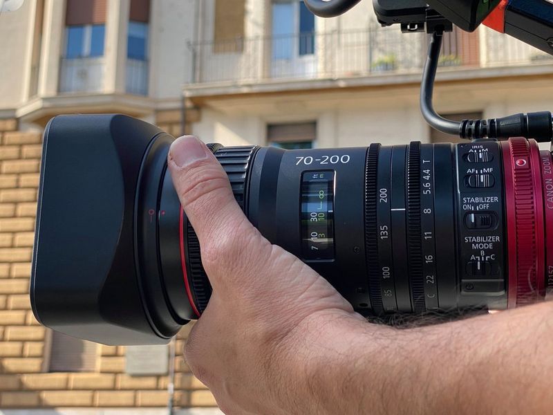 Un primo piano di un obiettivo Canon CN-E70-200mm T4.4 L IS attaccato ad una videocamera tenuta a mano.