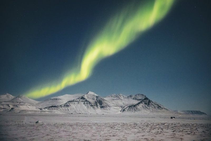 Green lights cross the sky, against a landscape of snow and mountains.