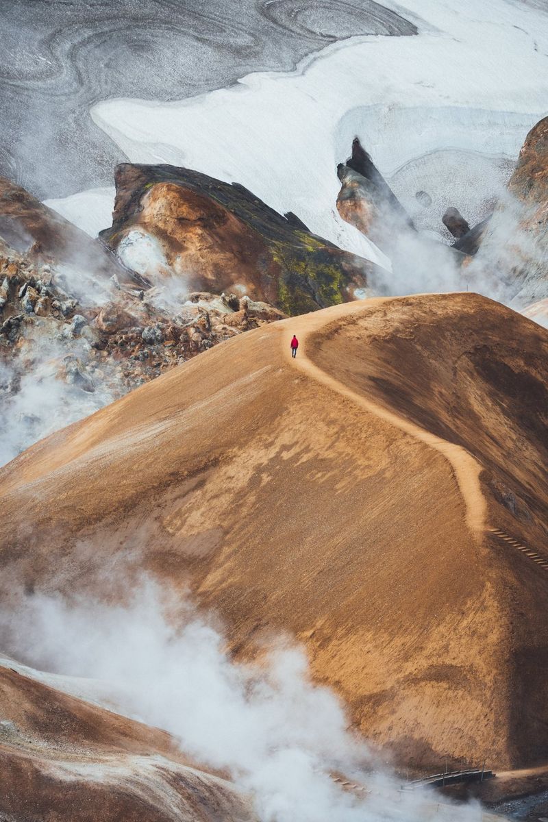 A figure is hiking along a mountain ridge, with mist swirling around the base of the mountain.