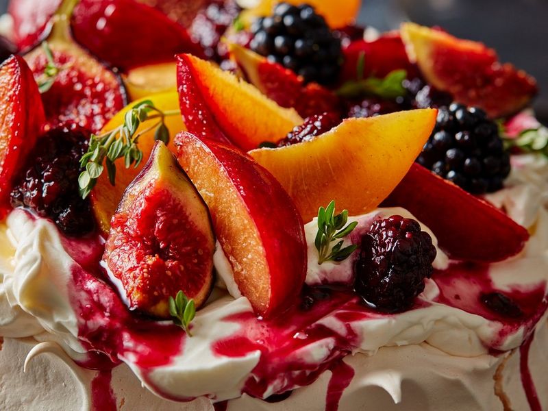 A close-up image of a pavlova, showing meringue, chopped nectarines, blackberries and figs, covered in a red fruit sauce.