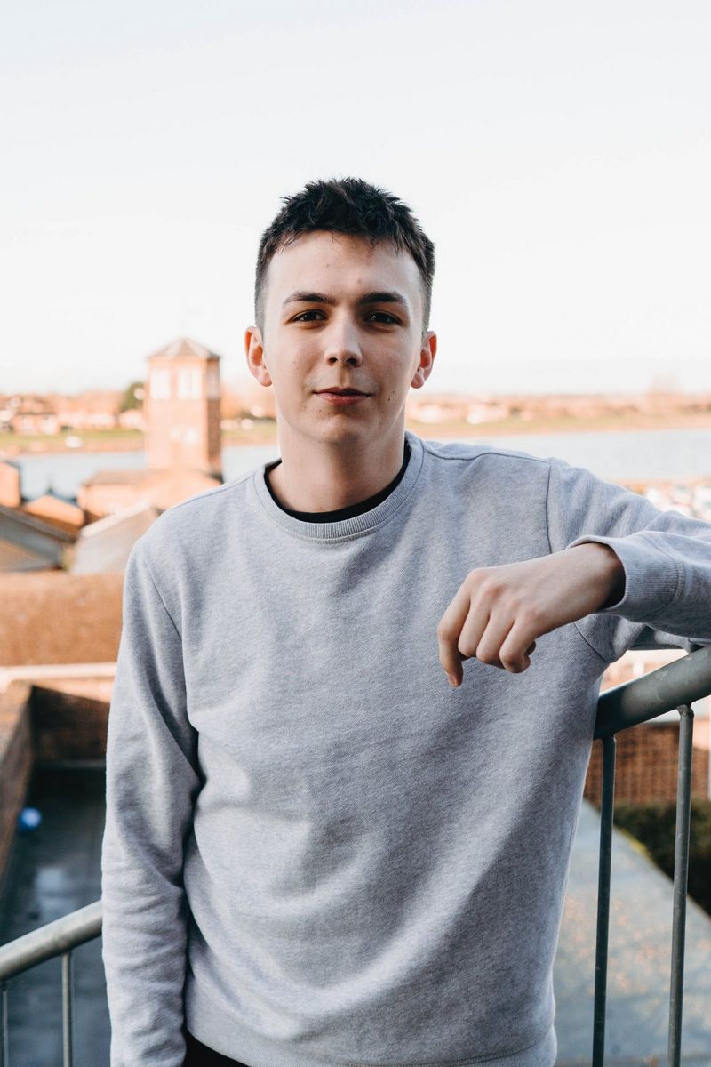 Харри Ситон, создатель контента и маркетинговый директор, в сером свитере позирует для камеры на уличной лестнице.