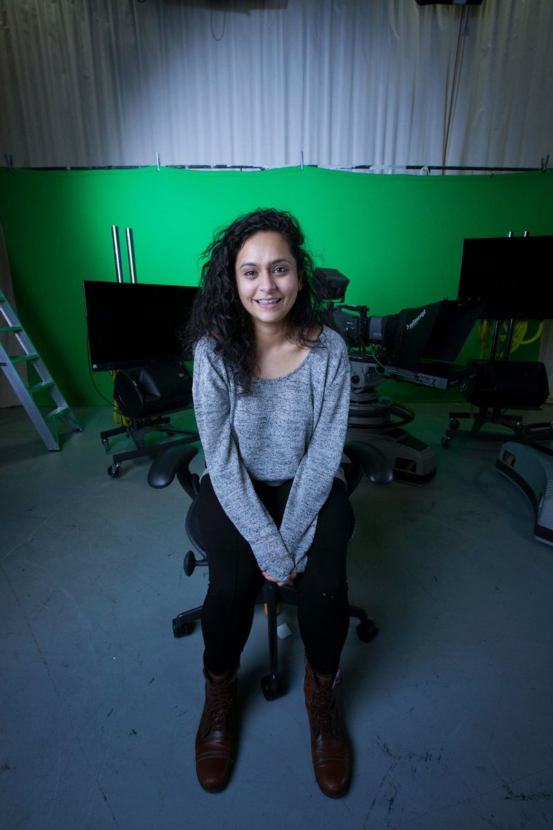 Продюсер и режиссер Жита Митра сидит на офисном стуле и улыбается, смотря в камеру.