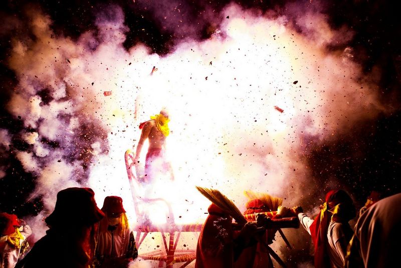 In una foto scattata da Jérôme Gence, una figura è illuminata dalla luce intensa provocata dall'esplosione di fuochi d'artificio, con il fumo che l'avvolge su uno sfondo scuro.