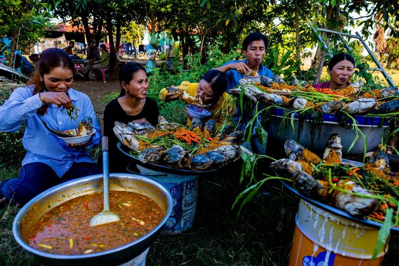 In una foto scattata da Jérôme Gence, quattro persone sono sedute all'esterno e mangiano attorno a una grande pentola e piatti di cibo.