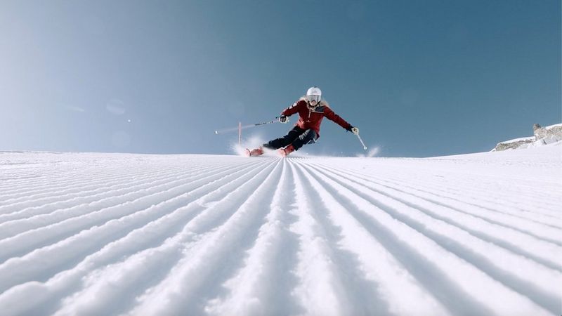 A video still of a person skiing at speed down a steep slope directly towards the camera. 