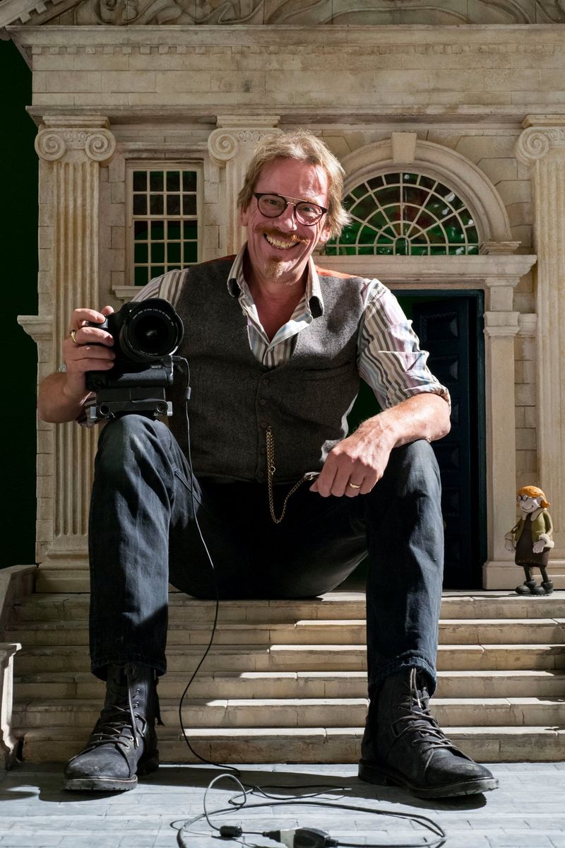Cinematographer Dave Alex Riddett sits on the steps of a model building.