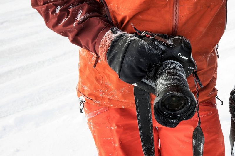 A gloved hand holding a Canon camera with a lens hood attached to protect it from the wintry conditions.