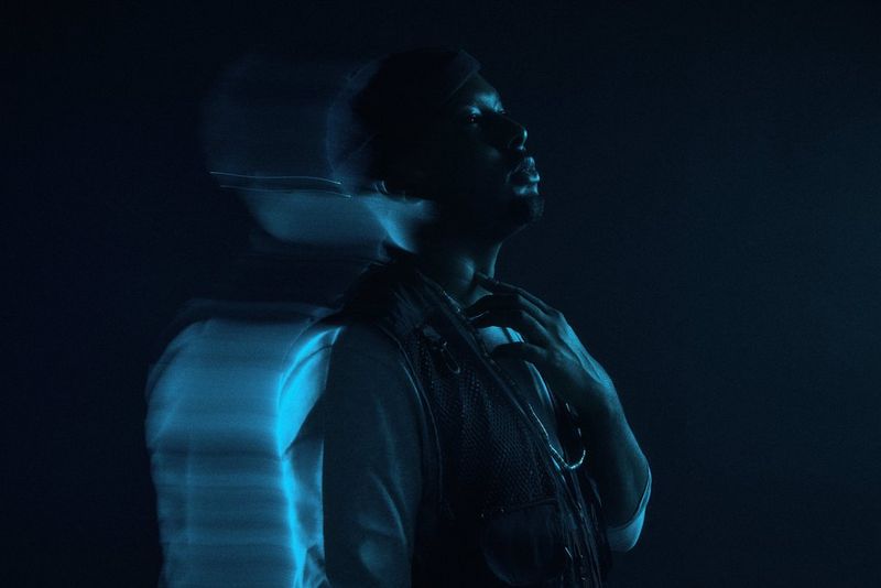 A portrait of dancer, artist and musician Tyrone Isaac-Stuart standing against a dark background taken on a Canon EOS R5.