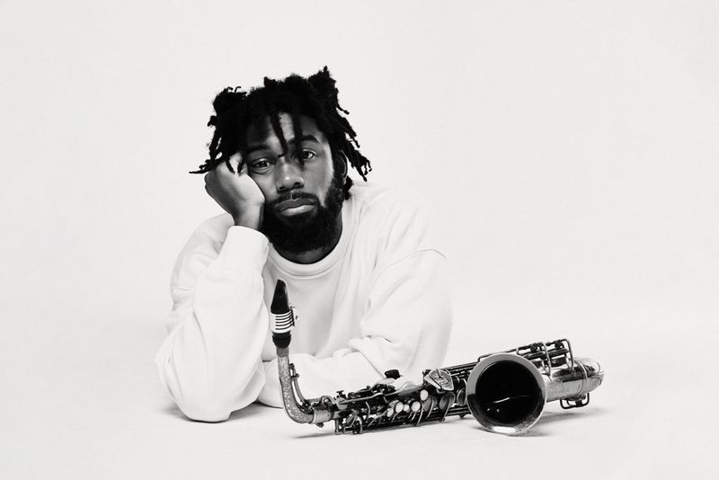 A black and white portrait, taken on a Canon EOS R5, of a figure in white resting their cheek on their hand, a saxophone in front of them.