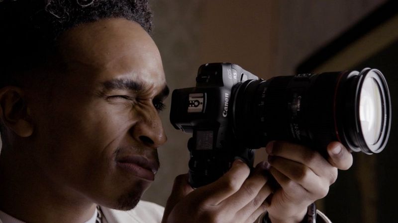 Fashion photographer Ian Hippolyte holding a Canon EOS R5 camera up to his eye.