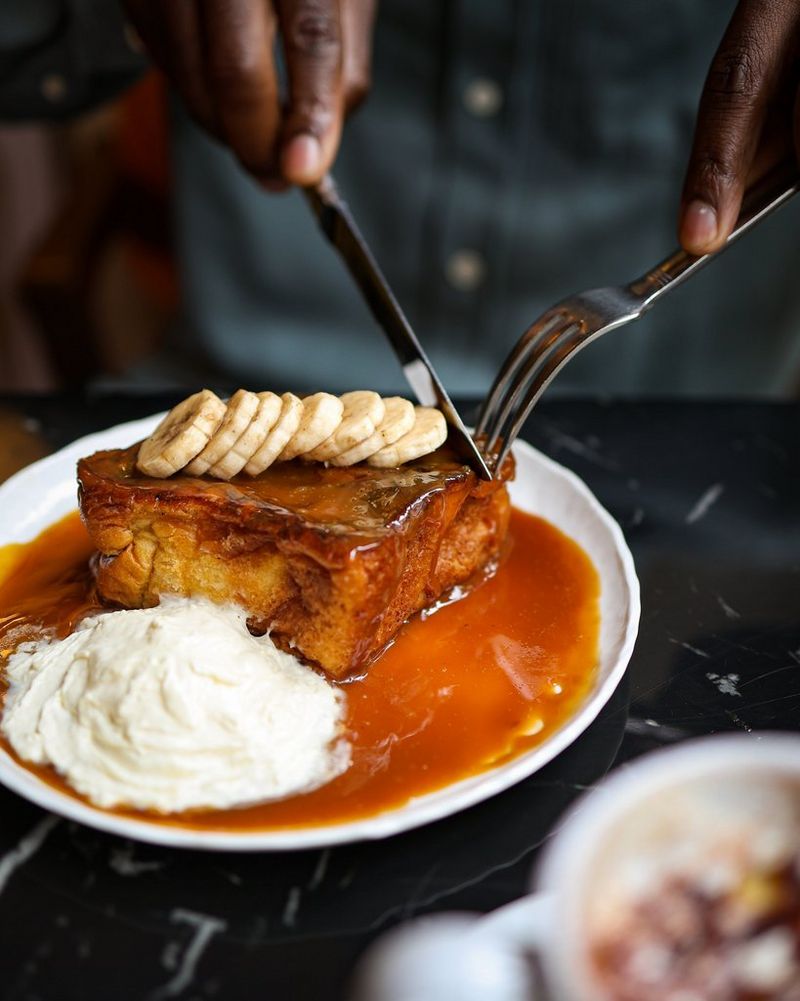 A close-up of a slice of pudding on a plate, next to a scoop of cream and coated in banana slices and syrup, in a shot taken by Laura Hannoun.