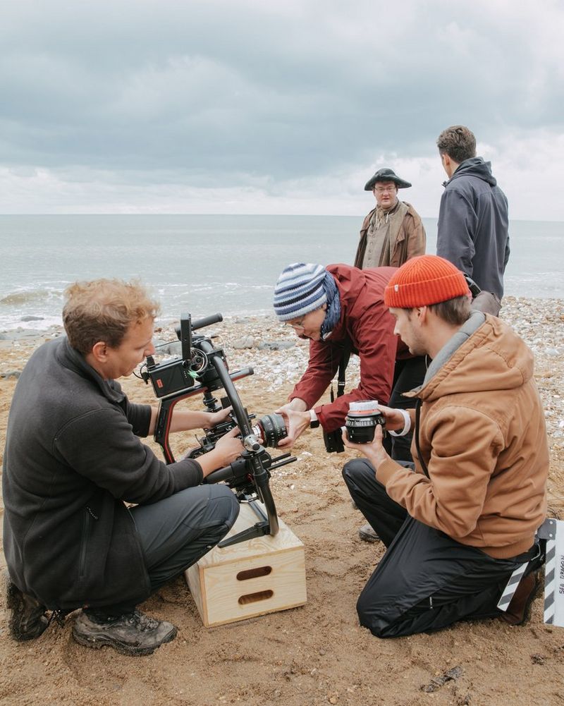 The Sea Dragon camera crew attaching a Sumire Prime lens to a camera on a beach.