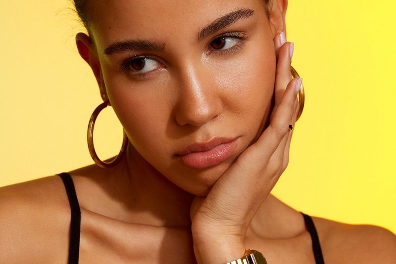 Gros plan d'un mannequin sur fond jaune posant la main sur sa joue. Photo prise par Laura Knipsael avec un Canon EOS R5.