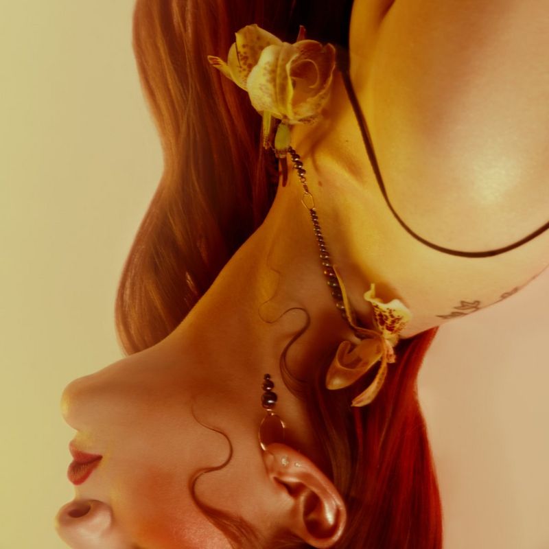 Portrait renversé du visage d'une personne, du nez vers le bas, son cou et ses épaules baignés d'une douce lueur jaune, avec une fleur suspendue à un collier. Photographie de Laura Knipsael.