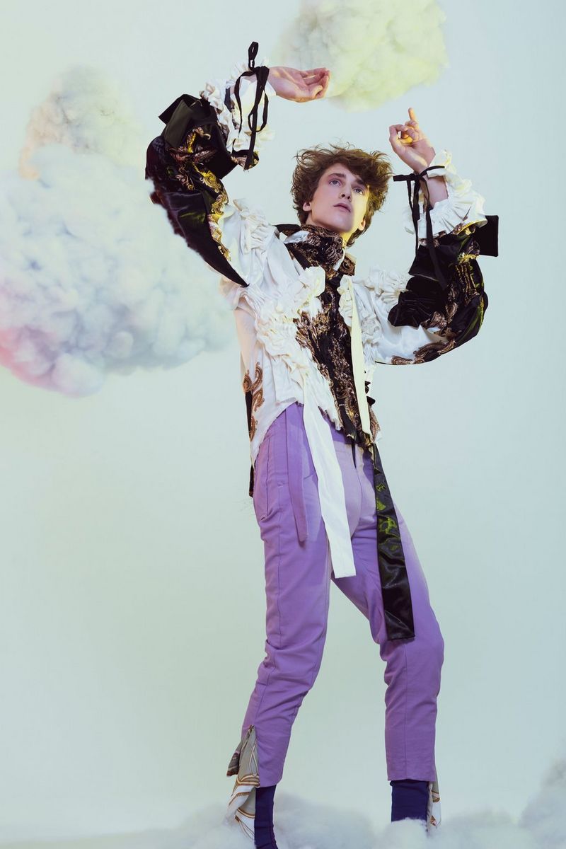 Une personne lève les bras comme pour se protéger, des nuages aux couleurs pastel derrière elle. Photographie de Laura Knipsael.