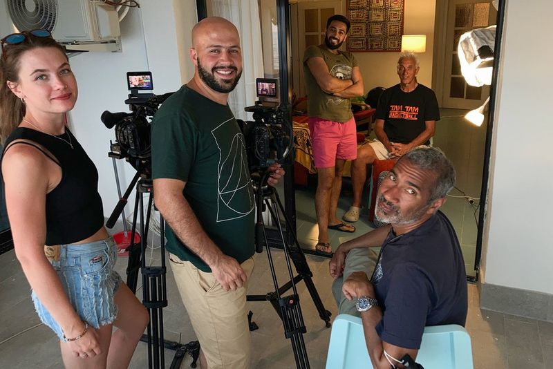 Un gruppo di persone al lavoro con due videocamere su dei treppiedi guarda verso la fotocamera.